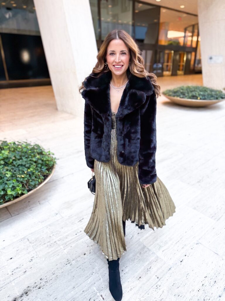 Woman in gold dress and black faux fur jacket ready for a show on broadway for NYC family trip