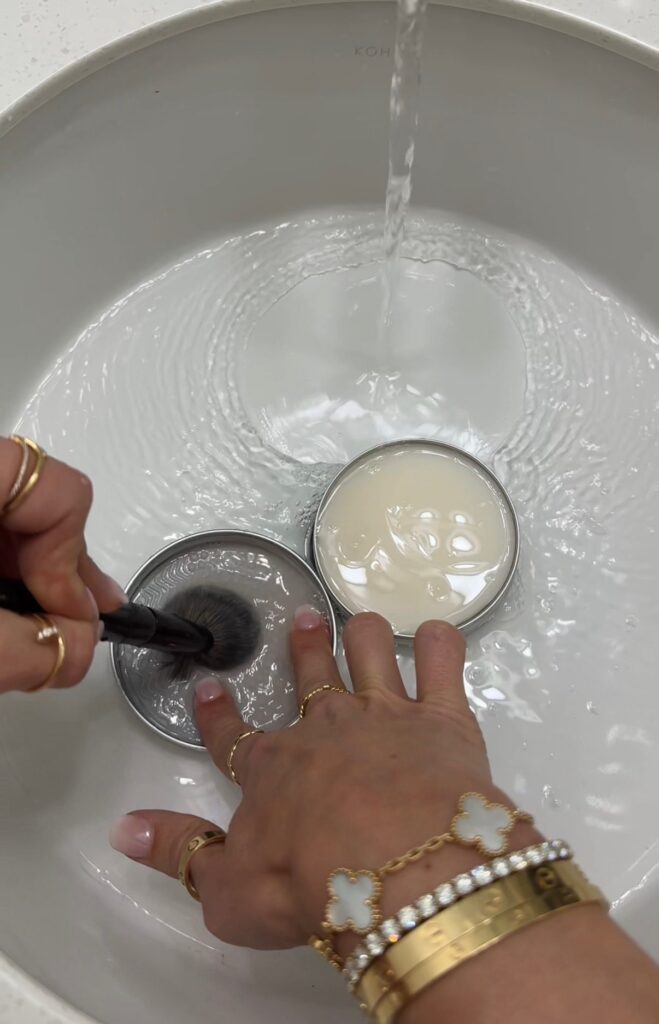 Hands cleaning makeup brushes with soap in a sink