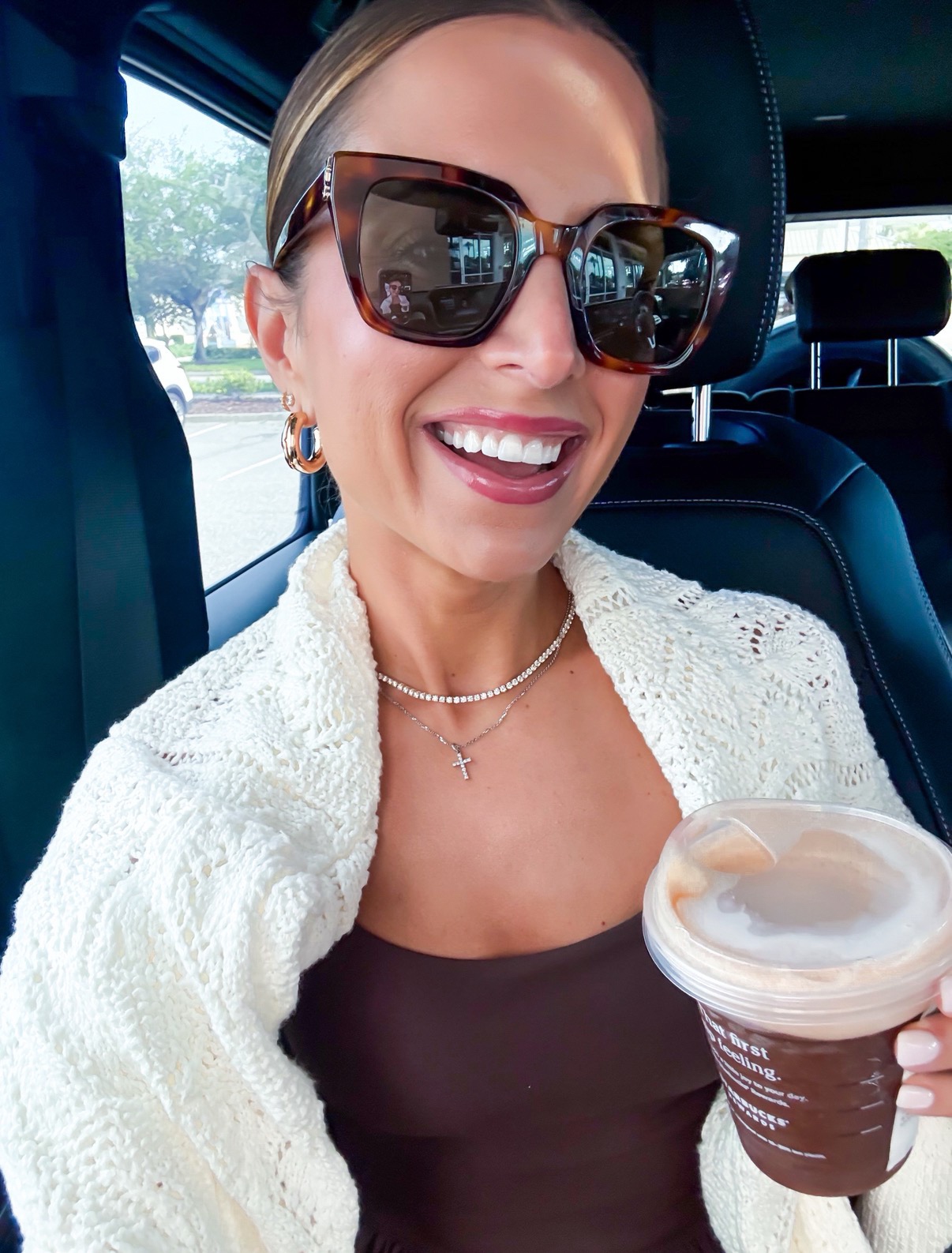 Brunette woman with sunglasses in car holding coffee