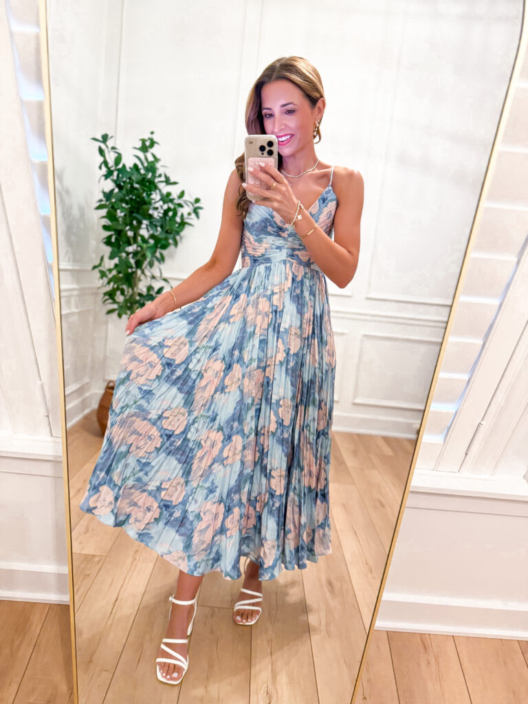 woman in mirror wearing blue and pink floral pleated dress as wedding guest dress