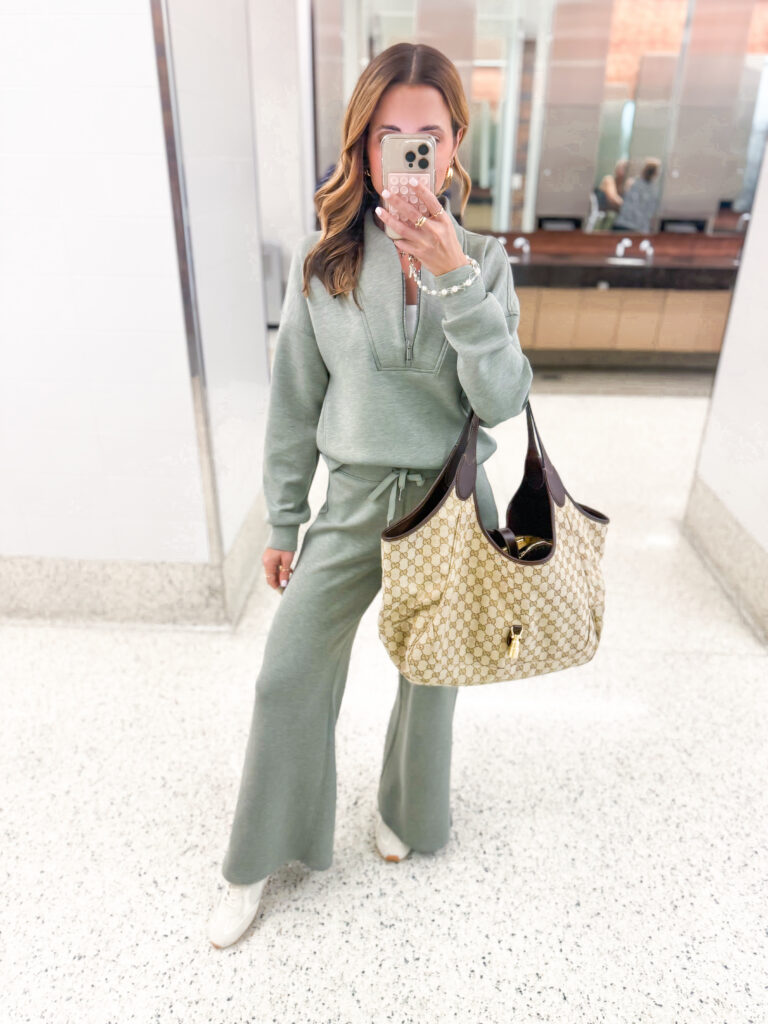 brunette influencer taking picture of green matching set travel outfit