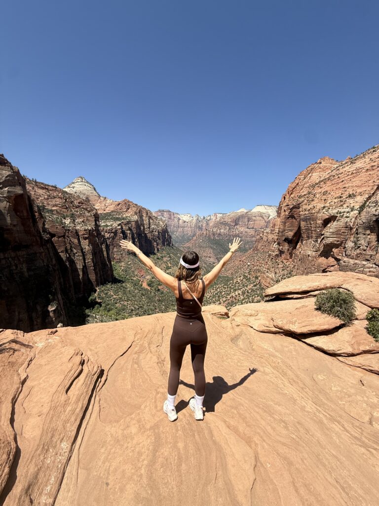 Brunette woman in matching brown yoga set facing view of Canton Overlook Trail in Zion